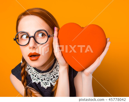 Nerd redhead girl with heart shape on yellow backgorund. Nerd redhead girl with heart shape on yellow backgorund. 45778042
