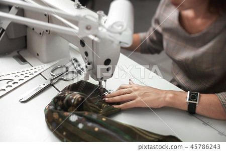 Seamstress working on modern electrical sewing machine making exclusive garments in fashion studio. Seamstress working on modern electrical sewing machine making exclusive garments in fashion studio. 45786243