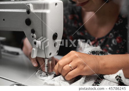 Seamstress hands connecting white fabric embroidered details with stripes of lace on sewing machine. Seamstress hands connecting white fabric embroidered details with stripes of lace on sewing machine. 45786245