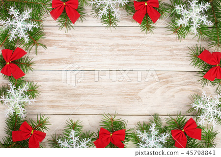 Christmas frame made of fir branches decorated with snowflakes and red bows on a light wooden 45798841