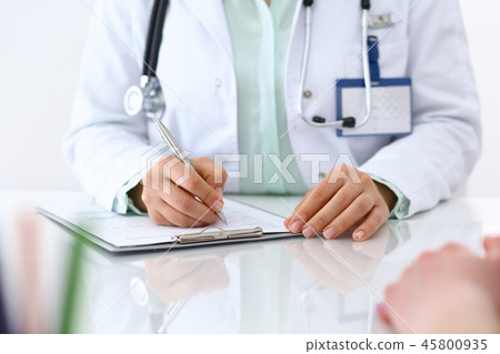 Doctor woman consulting patient while filling up an application form at the desk in hospital. Just Doctor woman consulting patient while filling up an application form at the desk in hospital. Just 45800935