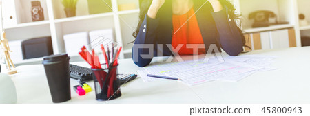 A beautiful young girl sits in the office at the table and holds her hands behind her head. 45800943