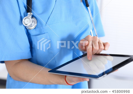 Woman doctor using tablet computer while standing straight in hospital office, closeup. Healthcare 45800998