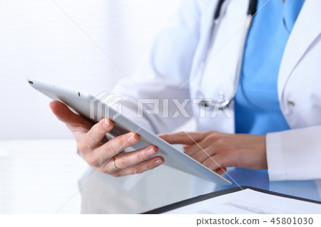 Woman doctor using tablet computer while sitting at the desk in hospital office, closeup. Healthcar Woman doctor using tablet computer while sitting at the desk in hospital office, closeup. Healthcar 45801030