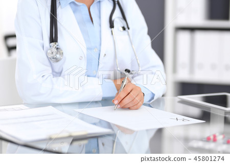 Doctor woman filling up prescription form while sitting at the desk in hospital close-up.  Physicia 45801274