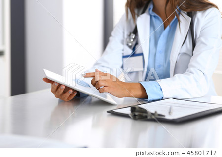 Unknown doctor woman using tablet computer while standing straight near window in hospital, close-up Unknown doctor woman using tablet computer while standing straight near window in hospital, close-up 45801712