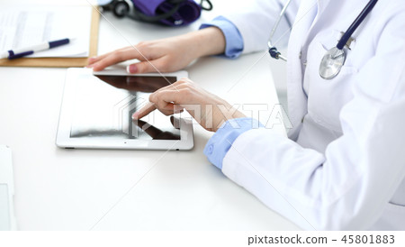 Woman doctor using tablet computer while sitting in hospital office closeup. Healthcare, insurance Woman doctor using tablet computer while sitting in hospital office closeup. Healthcare, insurance 45801883