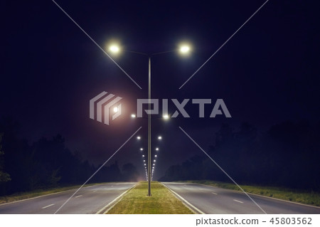 a two way road is illuminated by the light post 45803562