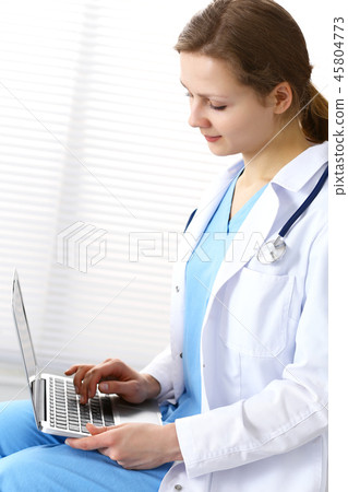 Woman doctor typing on laptop computer while working in hospital office. Data in medicine and health Woman doctor typing on laptop computer while working in hospital office. Data in medicine and health 45804773