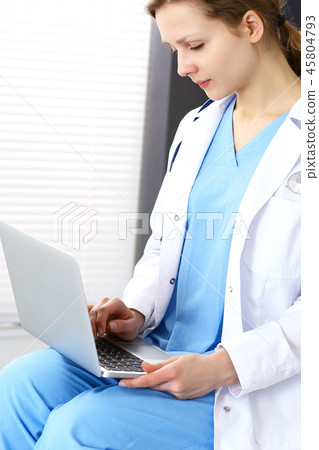 Woman doctor typing on laptop computer while working in hospital office. Data in medicine and health Woman doctor typing on laptop computer while working in hospital office. Data in medicine and health 45804793