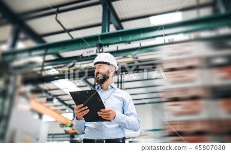 A portrait of an industrial man engineer with clipboard standing in a factory. 45807080