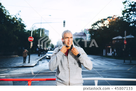 A portrait of an active mature man with earphones standing outdoors in city. 45807133