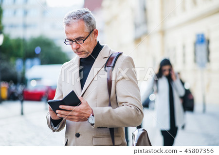 Mature businessman standing on a street in city, using smartphone. Mature businessman standing on a street in city, using smartphone. 45807356