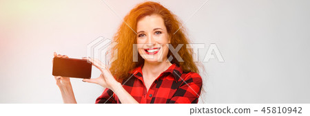 Young red-haired girl in a red checkered shirt. Young girl holding a phone Young red-haired girl in a red checkered shirt. Young girl holding a phone 45810942