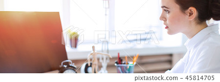 A young girl in the office sits at a table, works with a computer, calculator, documents and holds a 45814705