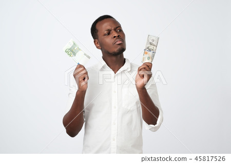 Young attractive african man holding USA currency and euro currency deciding which one to choose Young attractive african man holding USA currency and euro currency deciding which one to choose 45817526