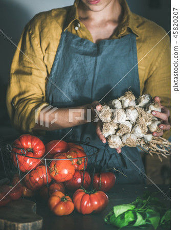 Woman in apron holding bunch of garlic for cooking Woman in apron holding bunch of garlic for cooking 45820207