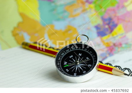 Compass notebook and pencil laid on a paper map. 45837692