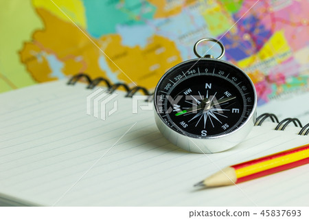 Compass notebook and pencil laid on a paper map. 45837693