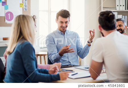 Group of young businesspeople sitting around table in a modern office, having meeting. Group of young businesspeople sitting around table in a modern office, having meeting. 45841601