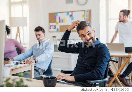 Young businessman in wheelchair with colleagues in a modern office. 45841603