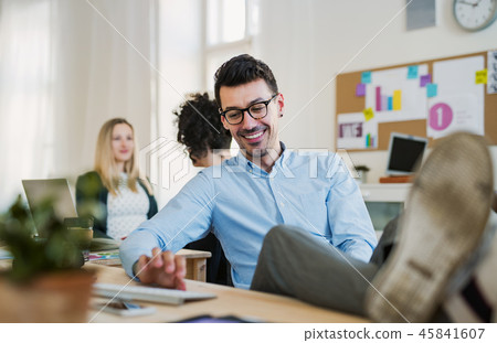 A portrait of young businessman with feet on table in a modern office. A portrait of young businessman with feet on table in a modern office. 45841607