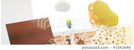Beautiful young girl sits in headphones and with a notepad at the table in the office and speaks 45842646