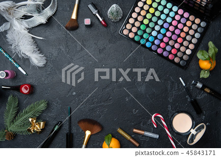 Photo of Christmas tree, mandarin, brushes, lipstick, palette with shadows on black table 45843171