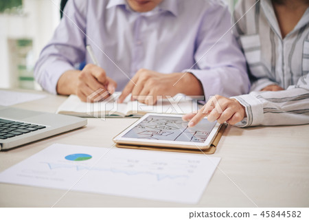 Crop colleagues using tablet while writing in notepad 45844582