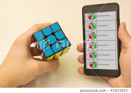 Cube puzzle in the left hand and the mobile phone on the right with the image of the scheme Jessica Cube puzzle in the left hand and the mobile phone on the right with the image of the scheme Jessica 45853055