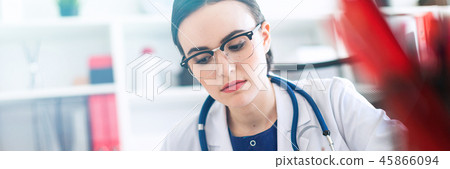 A beautiful young girl in a white robe is sitting at the computer desk with a marker and a book. A 45866094