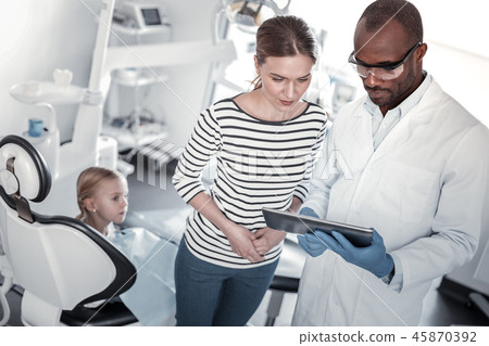 Attentive young woman standing near professional dentist Attentive young woman standing near professional dentist 45870392
