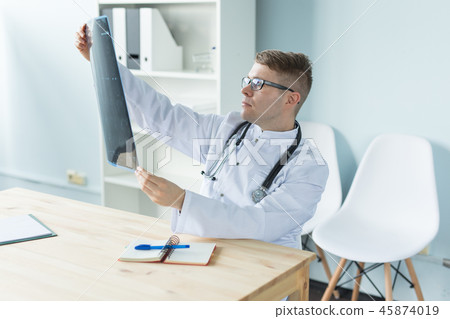 Healthcare, medical and people concept - doctor examines an x-ray sitting behind a desk Healthcare, medical and people concept - doctor examines an x-ray sitting behind a desk 45874019