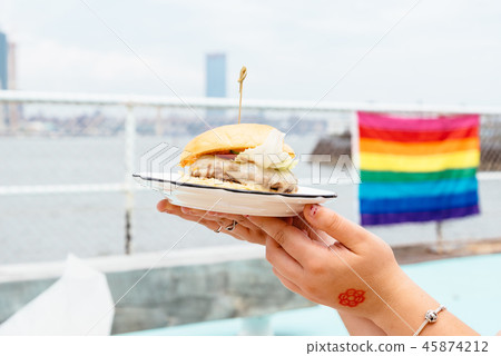 Woman holding burger with rainbow flag on background Woman holding burger with rainbow flag on background 45874212