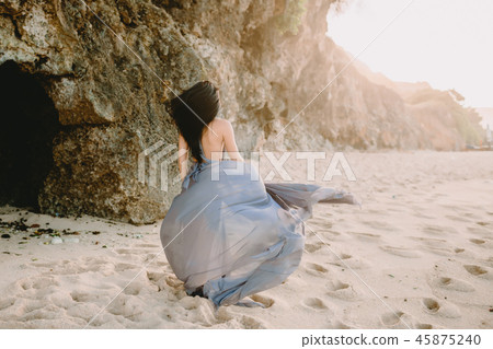 Woman in stylish blue dress in beach at sunset Woman in stylish blue dress in beach at sunset 45875240