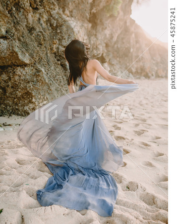 Woman in stylish blue dress in beach at sunset Woman in stylish blue dress in beach at sunset 45875241