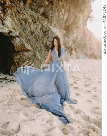 Woman in stylish blue dress in beach at sunset Woman in stylish blue dress in beach at sunset 45875242