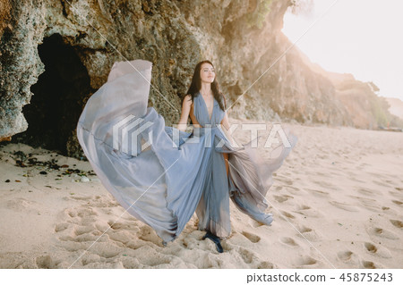 Woman in stylish blue dress in beach at sunset Woman in stylish blue dress in beach at sunset 45875243