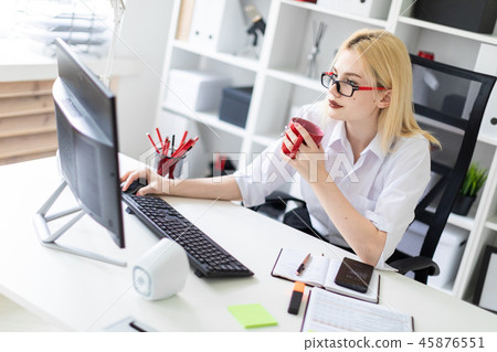 A young girl working at a computer in the office and holding a red Cup. 45876551