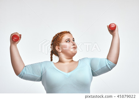 Funny red haired, chubby woman is smiling and holding dumbbells Funny red haired, chubby woman is smiling and holding dumbbells 45879022