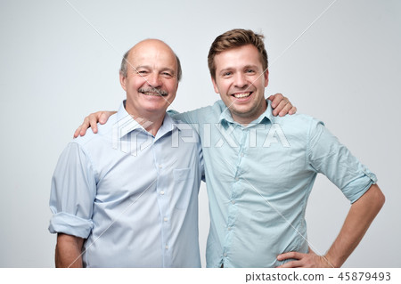 Hispanic father and adult son hugging and smiling at camera. 45879493