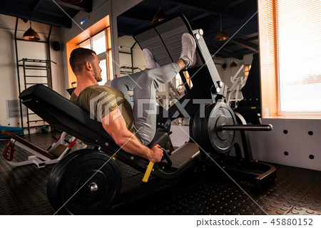 Young sporty man does leg exercises in gym side view Young sporty man does leg exercises in gym side view 45880152