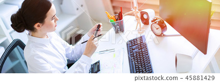 A young girl in the office sits at a table, holds a marker and a pencil in her hand and works with a A young girl in the office sits at a table, holds a marker and a pencil in her hand and works with a 45881429