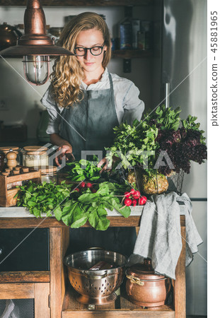 Young woman cutting herbs and vegetables in kitchen Young woman cutting herbs and vegetables in kitchen 45881965