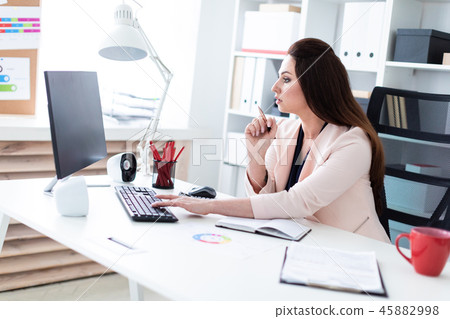 A young girl sitting at a computer Desk, holding a pen and working with a chart and a computer. 45882998