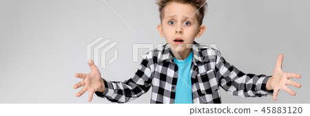 A handsome boy in a plaid shirt, blue shirt and jeans stands on a gray background. The boy spread A handsome boy in a plaid shirt, blue shirt and jeans stands on a gray background. The boy spread 45883120