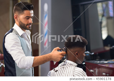 View from side of barber doing trendy haircut in barber shop View from side of barber doing trendy haircut in barber shop 45901178