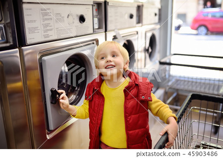 Little boy loads clothes into the washing machine 45903486