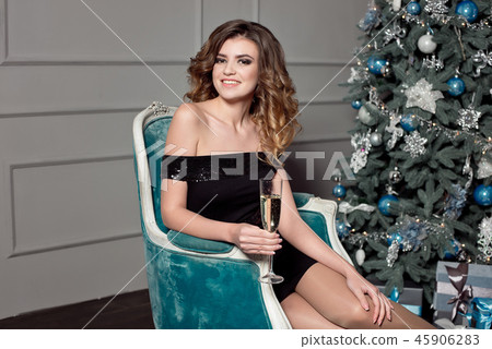 A young girl with gorgeous wavy hair, bright makeup, holds in her hands a glass of champagne, sits 45906283