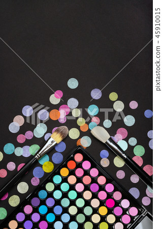 Cosmetic background with makeup brushes and eyeshadow palette on a black background with scattered Cosmetic background with makeup brushes and eyeshadow palette on a black background with scattered 45910015